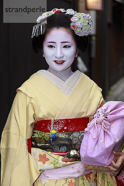 Lächelnde Maiko  Geisha-Lehrling  mit gelben Gewändern  hält auf der Straße auf dem Weg zu einer abendlichen Verabredung  Gion  Kyoto  Japan  Asien