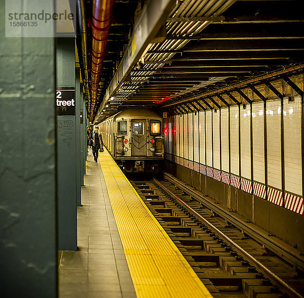 U-Bahn auf Schienen mit Menschen  die auf dem Bahnsteig gehen; New York City  New York  Vereinigte Staaten von Amerika