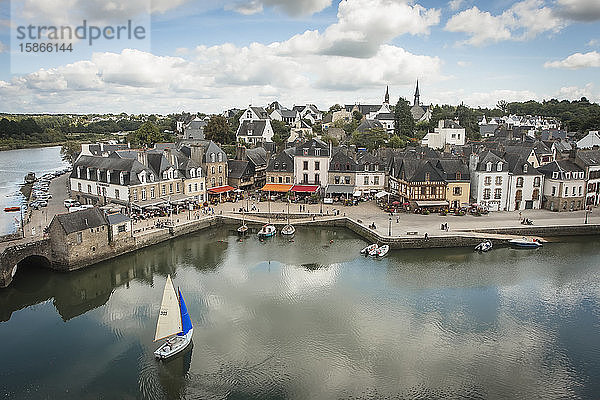 Ein kleines Segelboot mit einem blau-weißen Segel nähert sich dem Hafen von Saint Gustan  einer alten Hafenstadt mit traditionellen Gebäuden; Saint Gustan  Bretagne  Frankreich