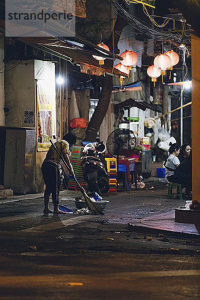 Frau kehrt nachts den Müll auf der Straße auf; Hanoi  Veitnam
