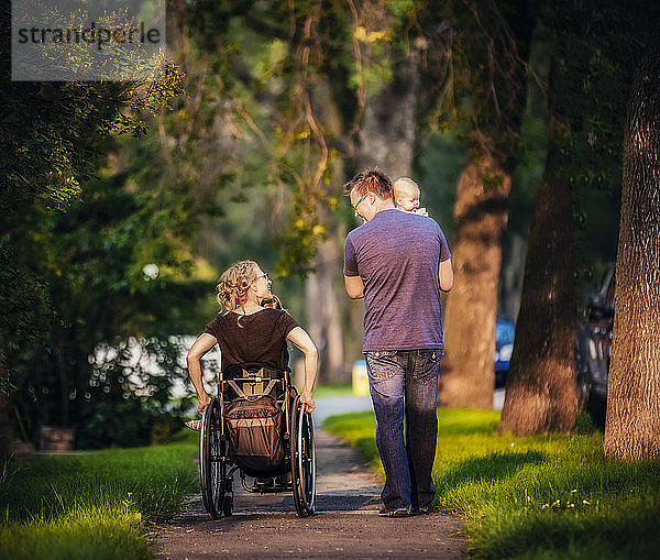 Blick von hinten auf eine Familie  die abends spazieren geht; die Mutter ist querschnittsgelähmt und sitzt im Rollstuhl; Edmonton  Alberta  Kanada