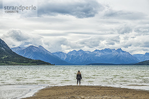 Frau steht an einem Sandstrand und blickt auf den Carcross Lake und die weiten Yukon Ranges; Carcross  Yukon  Kanada