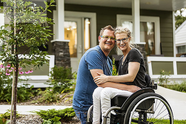 Ein Ehemann und seine querschnittsgelähmte Frau posieren an einem warmen Herbsttag für ein Familienfoto in ihrem Vorgarten: Edmonton  Alberta  Kanada