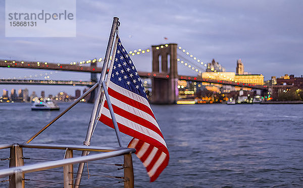 Eine amerikanische Flagge weht an einem Geländer an der Uferpromenade mit Blick auf die Brooklyn Bridge  Manhattan; New York City  New York  Vereinigte Staaten von Amerika