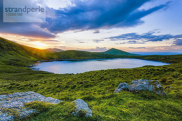 Sonnenuntergang über dem Lough Muskery in den Galty Mountains im Sommer mit großen Felsbrocken im Vordergrund  Galty Mountains; Grafschaft Limerick  Irland