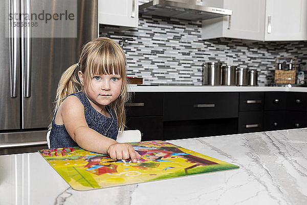 Ein süßes kleines Mädchen  das in der Küche ein Buch liest und in die Kamera schaut: Edmonton  Alberta  Kanada