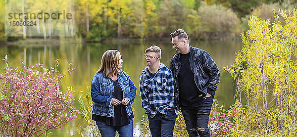 Ein junger Mann mit Down-Syndrom geht mit seinem Vater und seiner Mutter an einem warmen Herbstabend in einem Stadtpark spazieren und genießt die Gesellschaft des anderen: Edmonton  Alberta  Kanada