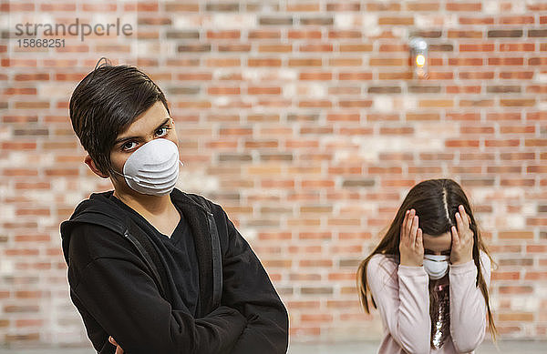 Geschwister  die während der weltweiten Coronavirus-Pandemie Schutzmasken zum Schutz vor COVID-19 tragen  der Junge mit verschränkten Armen  das Mädchen mit Händen  die sich aus Angst den Kopf halten; Toronto  Ontario  Kanada