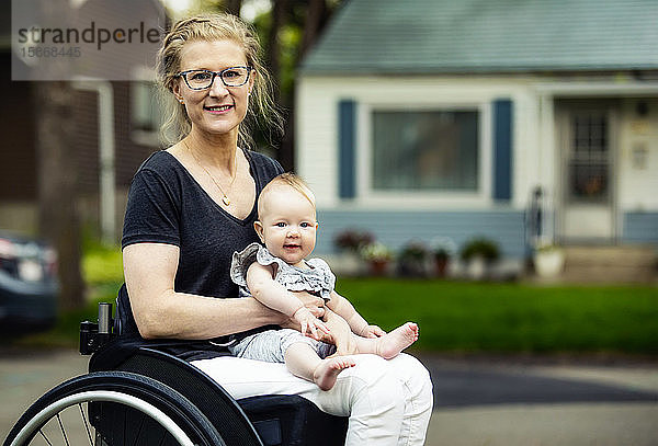 Eine querschnittsgelähmte Mutter  die ihr Baby auf dem Schoß trägt  während sie einen Rollstuhl benutzt  an einem warmen Sommernachmittag im Freien: Edmonton  Alberta  Kanada