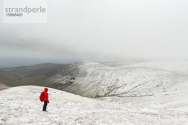 Wanderin in roter Jacke beim Wandern auf einem schneebedeckten Berg im Winter bei schlechtem Wetter  Galty Mountains; County Tipperary  Irland