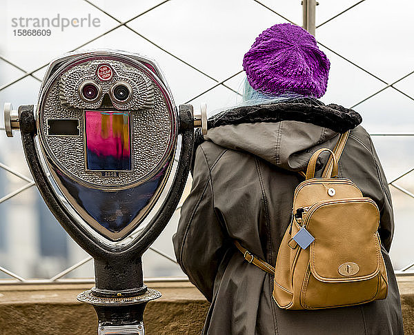 Weibliche Touristin steht neben einem Fernglas auf der Aussichtsplattform des Empire State Building in Midtown Manhattan; New York City  New York  Vereinigte Staaten von Amerika