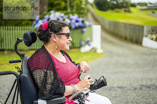 Maori-Frau mit Cerebralparese in einem Rollstuhl  die einen Bürgersteig entlangfährt; Wellington  Neuseeland