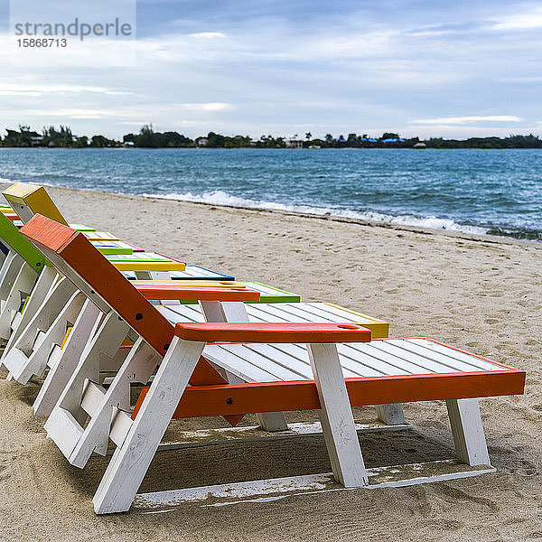 Bunte Liegestühle am Strand in einer Reihe auf dem Sand am Rande des Wassers  Placencia Peninsula; Placencia  Belize