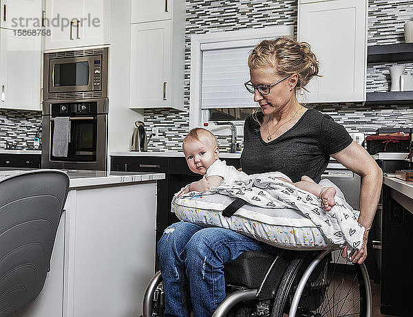 Eine querschnittsgelähmte Mutter hält ihr Baby in der Küche auf dem Schoß  während sie ihren Rollstuhl schiebt: Edmonton  Alberta  Kanada
