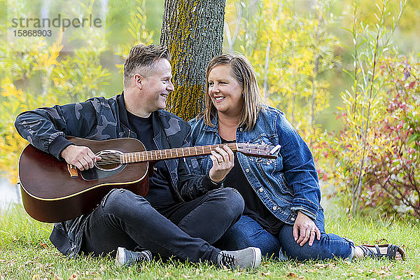 Ein reifes Paar verbringt viel Zeit miteinander  und die Frau hört ihrem Mann beim Singen und Gitarrenspiel zu  während sie an einem warmen Herbstabend in einem Stadtpark ist: Edmonton  Alberta  Kanada