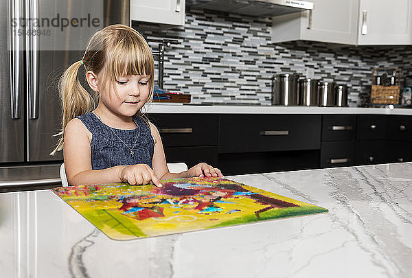 Ein süßes kleines Mädchen  das in der Küche ein Bilderbuch liest und auf etwas zeigt  das ihre Aufmerksamkeit erregt: Edmonton  Alberta  Kanada
