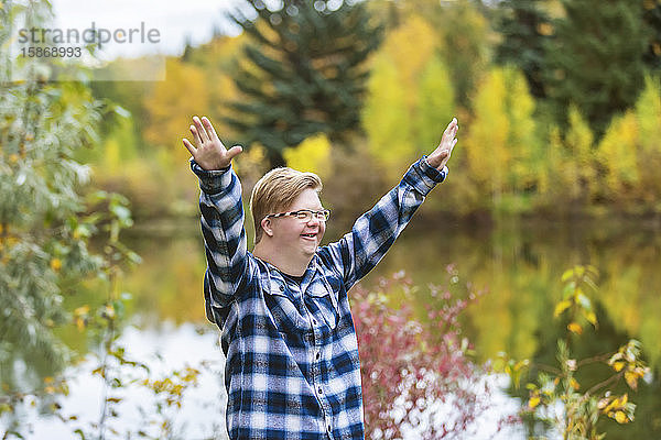Ein junger Mann mit Down-Syndrom hebt an einem warmen Herbstabend in einem Stadtpark seine Hände zur Anbetung Gottes: Edmonton  Alberta  Kanada