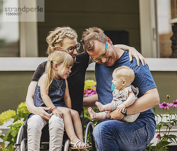 Eine junge Familie posiert für ein Familienporträt im Freien in ihrem Vorgarten  die Mutter ist querschnittsgelähmt und sitzt im Rollstuhl; Edmonton  Alberta  Kanada