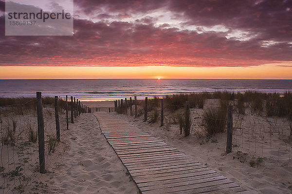 Holzsteg  der zu einem französischen Strand an der Atlantikküste mit untergehender Sonne im Sommer führt; Lacanau  Frankreich