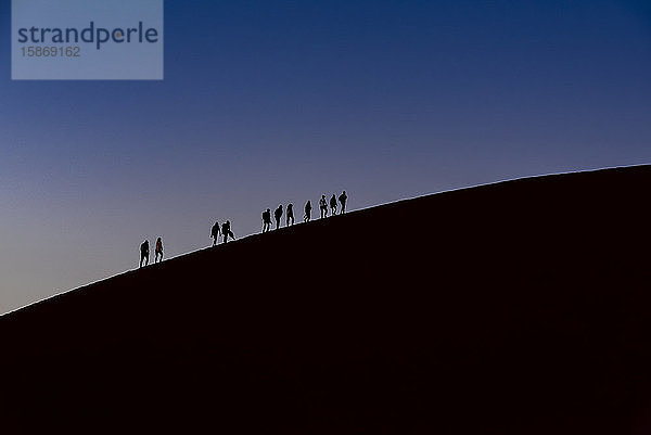 Silhouette von Touristen beim Besteigen der Düne 45 in der Abenddämmerung  Sossusvlei  Namib-Wüste; Namibia