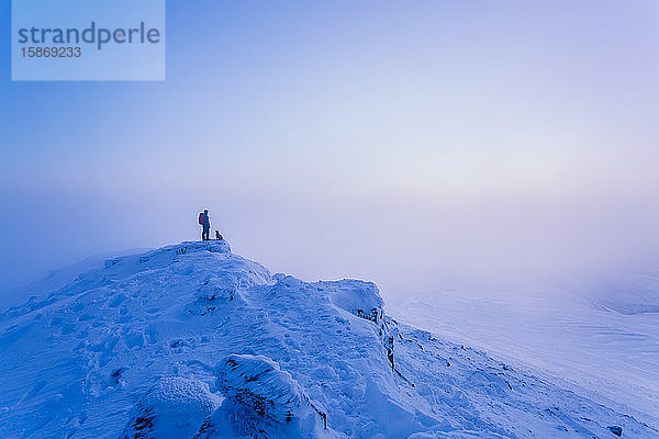 Mann und Hund wandern auf dem Gipfel eines schneebedeckten Berges im Winternebel  Galty Mountains; County Tipperary  Irland