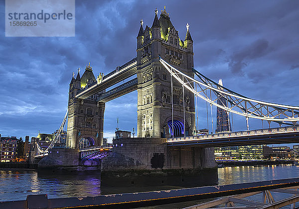 Tower Bridge beleuchtet in der Abenddämmerung und reflektiert im ruhigen Wasser der Themse; London  England