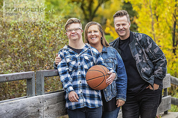 Ein junger Mann mit Down-Syndrom genießt mit seinem Vater und seiner Mutter an einem warmen Herbstabend die Gesellschaft des anderen in einem Stadtpark: Edmonton  Alberta  Kanada