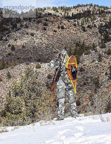 Jäger mit Tarnkleidung und Gewehr  der mit einem Fernglas im Winter nach draußen schaut; Denver  Colorado  Vereinigte Staaten von Amerika