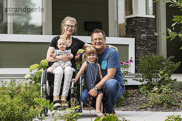 Eine junge Familie posiert für ein Familienporträt im Freien in ihrem Vorgarten  die Mutter ist querschnittsgelähmt und sitzt im Rollstuhl; Edmonton  Alberta  Kanada