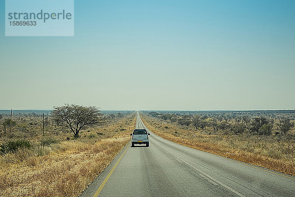 Ein Lastwagen fährt auf einer offenen Straße in der Wüste mit einem großen blauen Himmel am Horizont; Namibai