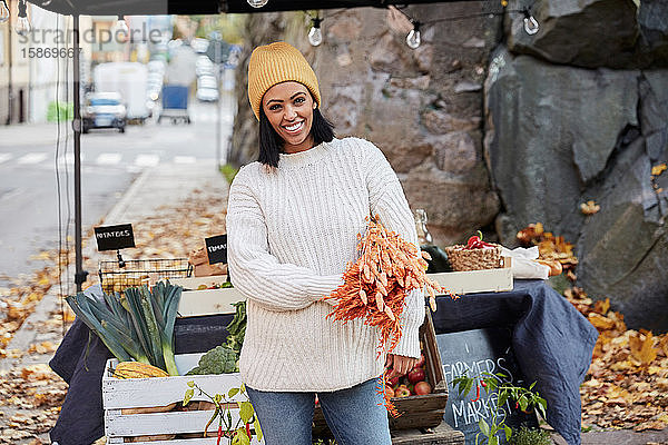 Porträt einer glücklichen Frau  die mit Feldfrüchten am Marktstand steht