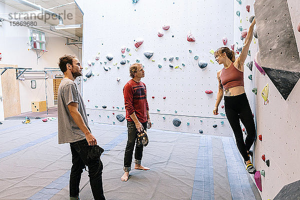 Frau klettert an der Wand  während sie den Ausbilder und den Schüler im Fitnessstudio betrachtet