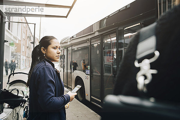 Mittlere erwachsene Frau  die während des Wartens auf den Bus in der Stadt ein Mobiltelefon benutzt