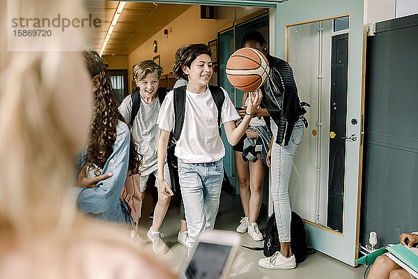 Spielerische männliche Schüler  die in der Mittagspause mit Basketball auf dem Schulkorridor laufen