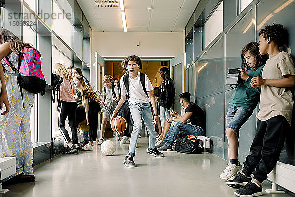 Männlicher Schüler spielt in der Mittagspause auf dem Schulkorridor mit Basketball