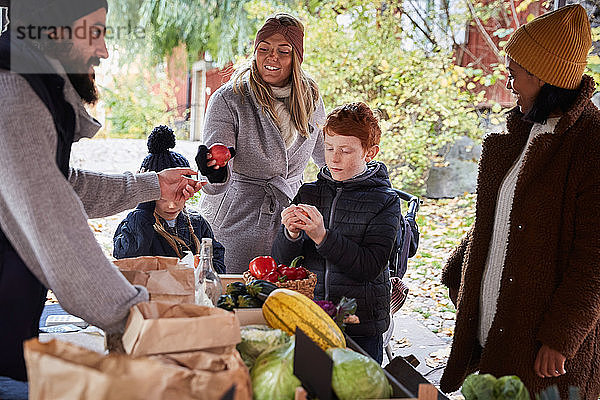 Lächelnde Frau kauft am Gemüsestand frische Äpfel von männlichem Marktverkäufer