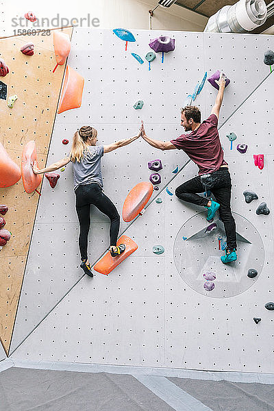 Rückansicht von Freundinnen und Freunden beim Abklatschen beim Klettern an der Kletterwand im Fitnessstudio