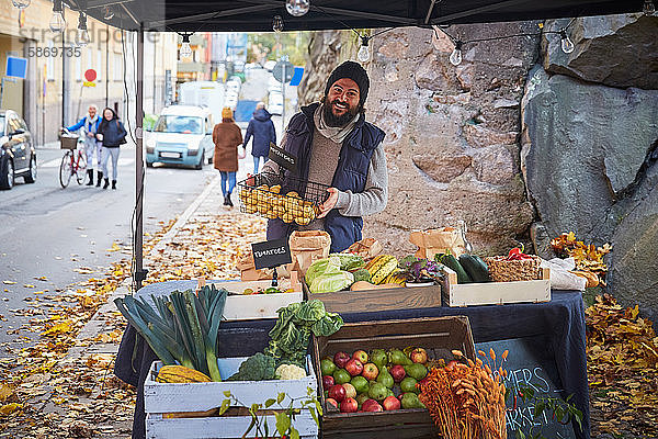 Porträt eines glücklichen Mannes stehend mit Gemüsekorb am Marktstand