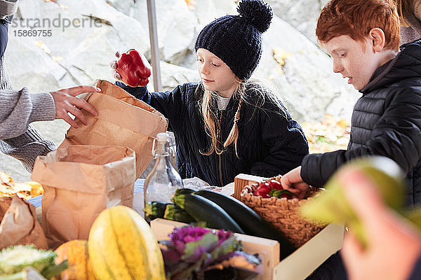 Mädchen kauft rote Paprika  während sie mit ihrer Familie am Marktstand steht