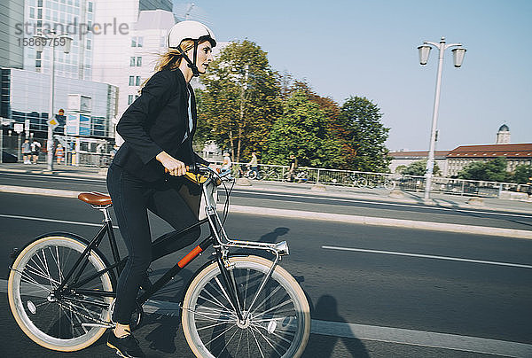 Seitenansicht einer Geschäftsfrau auf dem Fahrrad in der Stadt Straße gegen Himmel
