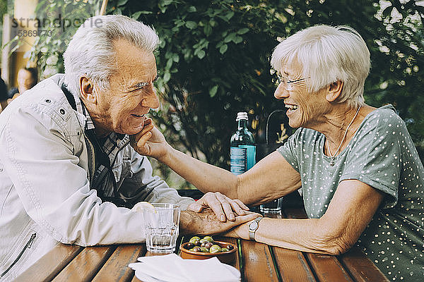 Lächelnde ältere Frau berührt die Wange ihres Partners  während sie in einem Restaurant in der Stadt sitzt