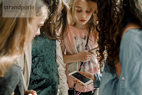 Schülerinnen  die auf das Telefon schauen  während sie im Schulflur stehen