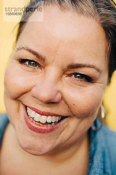 Nahaufnahme-Porträt einer lächelnden reifen Frau vor gelbem Hintergrund