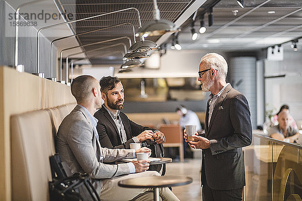 Leitender Geschäftsmann im Gespräch mit männlichen Kollegen während der Kaffeepause im Büro