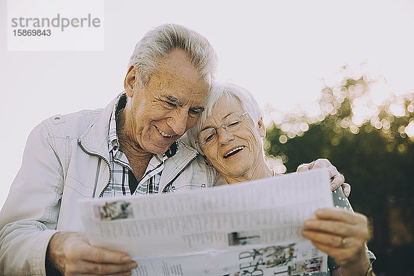 Lächelndes älteres Ehepaar liest Karte  während es im Urlaub in der Stadt steht