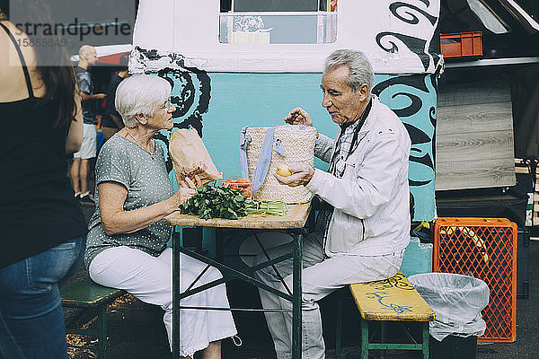Älterer Mann und Frau diskutieren über Gemüse  während sie auf einem Markt in der Stadt sitzen