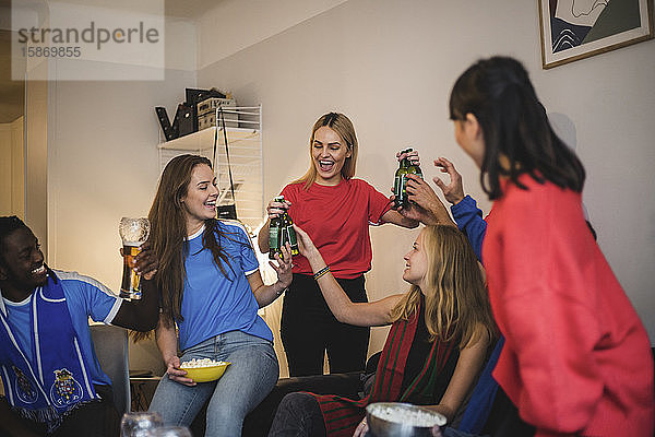 Glückliche Freunde halten Bierflaschen beim Genießen im Wohnzimmer