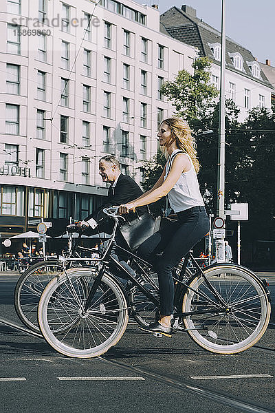 Männliche und weibliche Mitarbeiter fahren auf Straßenfahrrädern gegen Gebäude in der Stadt