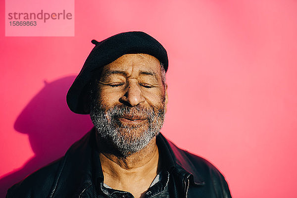 Lächelnder älterer Mann mit geschlossenen Augen vor rosa Hintergrund