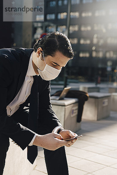 Geschäftsmann mit Gesichtsmaske sitzt draußen und telefoniert